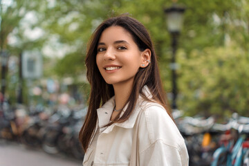 Radiating confidence, a young woman poses against the iconic backdrop of Amsterdam's charming streets, with bicycles weaving the essence of city life