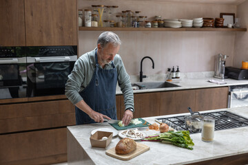 Mature retired male cooking in his kitchen preparing a meal