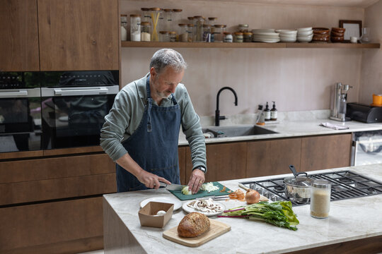 Mature retired male cooking in his kitchen preparing a meal
