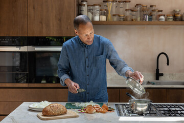 Mature retired male cooking a homemade meal in his kitchen