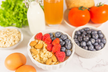 Healthy breakfeast concept. Oatmeal cereal porridge with fresh berries and nuts in white bowl, vegetable and juice. Dietary. Top view on white marble stone table. 