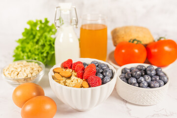Healthy breakfeast concept. Oatmeal cereal porridge with fresh berries and nuts in white bowl, vegetable and juice. Dietary. Top view on white marble stone table. 