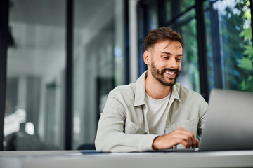 A smiling man, working over the laptop, at the office.