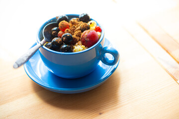 Healthy breakfast with cereal and berries in blue cup on wooden table