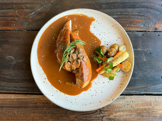 Sliced chicken steak with barbeque steak sauce, served with baby tomatoes and baby corns, with thyme and rosemary leaves. On white plate, on wooden rustic table
