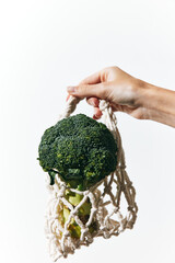 Person holding fresh broccoli with white netting bag and cloth on top