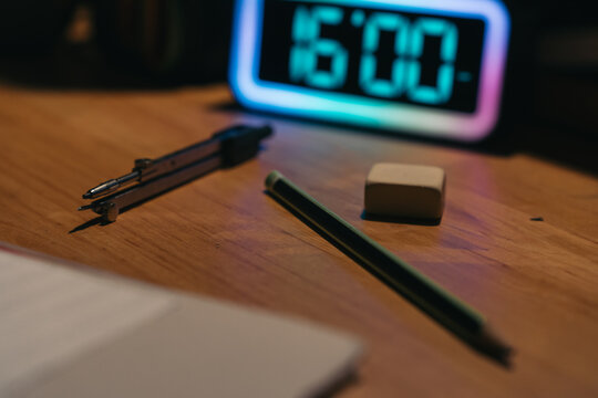 Student desk at night with clock showing 4pm. Geometry tools and pencil lying on student's desk with alarm clock showing 4pm