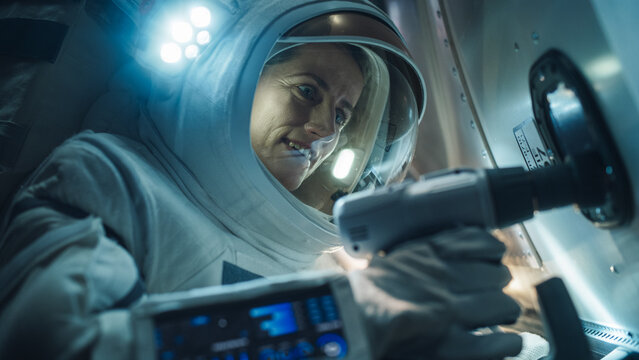 Close-Up Of Female Space Technician Mending a Panel on an International Space Station with an Automatic Screw Gun. Fearless Astronaut Working in Outer Space with Gorgeous Blue Planet in the Background
