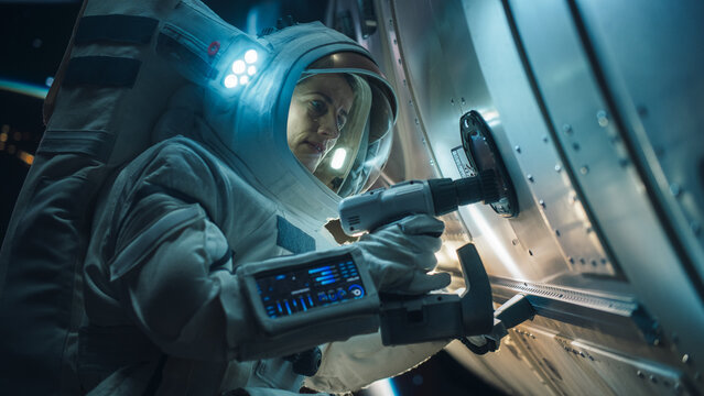 Space Engineer Servicing a Panel on a Communication Satellite with an Automatic Screw Gun. Brave Female Astronaut Working in Outer Space with Beautiful Blue Planet Earth in the Background