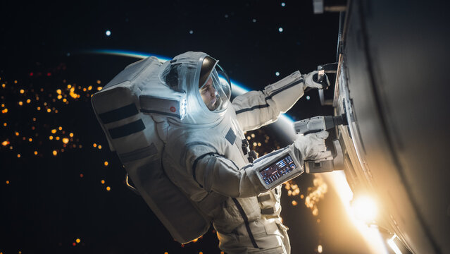 Space Engineer Servicing a Panel on a Communication Satellite with an Automatic Screw Gun. Brave Astronaut Working in Outer Space with Beautiful Dark Side of Planet Earth in the Background