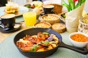 English Breakfast in cooking pan with fried eggs, sausages, bacon, mushrooms, beans and tomato