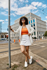 A woman in a white blazer and skirt poses on a European street.