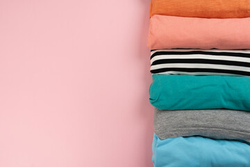 close up of rolled colorful t shirt clothes on pink table background, travel and lifestyle concept