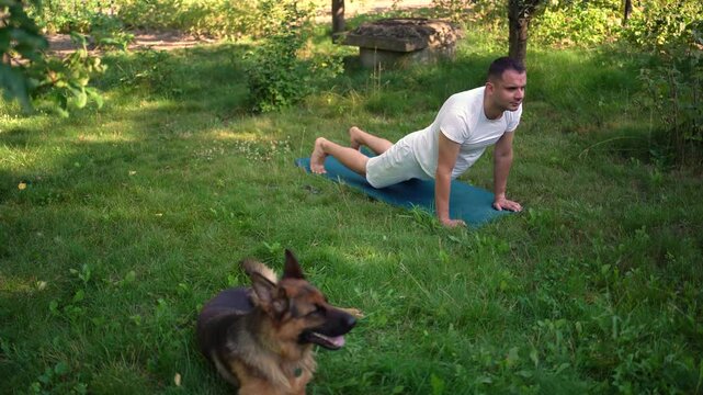 a man does somatic exercises with his dog in the garden in the morning