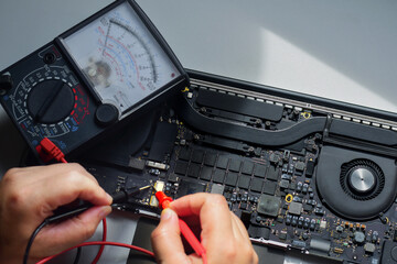 computer technician A laptop motherboard repairman is using an IC meter to find defects on the...