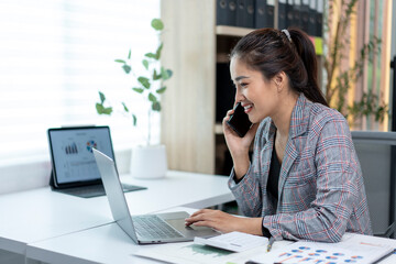 Obraz premium A woman is talking on her cell phone while sitting at a desk with a laptop