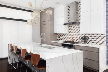 A modern kitchen with wood and white cabinets, chairs sitting at a marble waterfall island, and a...