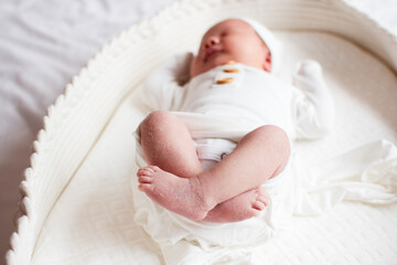 Little newborn baby sleeping in a bassinet in a white outfit and a hat. Newborn baby girl sleeping. Child care concept