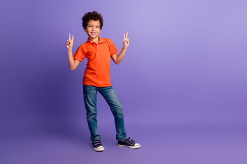 Full length photo of funky cool son dressed orange t-shirt showing two v-signs emtpy space isolated violet color background