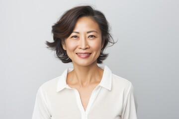 Fototapeta premium Portrait of a grinning asian woman in her 50s wearing a simple cotton shirt isolated in plain white digital canvas