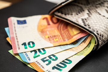 Close-up of Euro Banknotes Emerging from Stylish Leather Wallet on Dark Table, Focus on Detailed Currency Textures