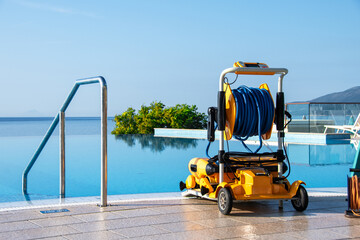 Modern Robotic Pool Cleaner by Blue Infinity Pool with Tropical Scenery, Outdoor Pool Maintenance Equipment in Sunlight