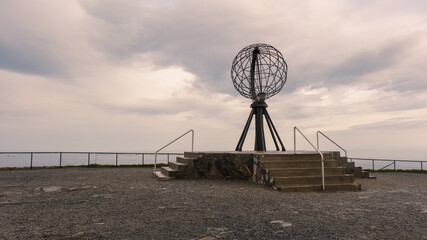 The iconic globe sculpture stands tall against a cloudy sky on a rocky outcrop overlooking the sea. Nordkapp or North Cape