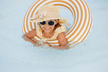 Cute funny toddler girl in swimsuit and sunglasses relaxing on inflatable toy ring floating in pool...