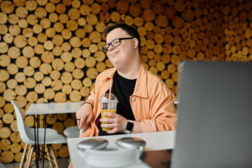 A man with Down syndrome enjoys a beverage while working on his laptop in a cafe.