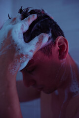 handsome young man washes himself under a cold shower in the bathroom. Drops of water flow down the...