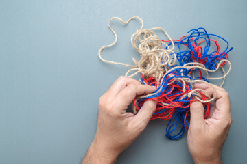 Hand trying to solve the problem of tangled jute ropes, confused circumstance, and psychotherapy...