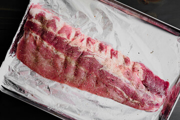 Raw Slab of Baby Back Ribs Seasoned with Salt and Pepper: Uncooked seasoned rack of pork ribs on a foil covered sheet pan