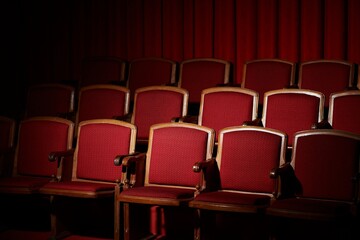 Rows of empty red velvet seats in a darkened movie theater, anticipation hangs in the air.