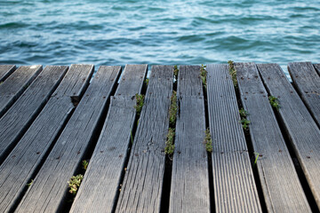 Fototapeta premium a wooden pier with grass growing out of it and water in the background