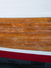 A pattern of stripes in white, red, black, and natural stain on the side of a boat.