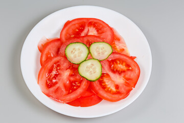 Sliced red tomato and cucumber on dish on gray background