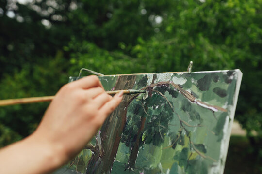 Close up of female artist's hands make a brush stroke on the canvas. Mindfulness, art therapy, creativity concept. Process of plein air painting in nature. Part of the series