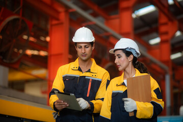 Latino male engineers industrial and female auditor wearing safety uniform workwear Walking to Audit and checking the safety of the work area and warehouse in an industrial factory.