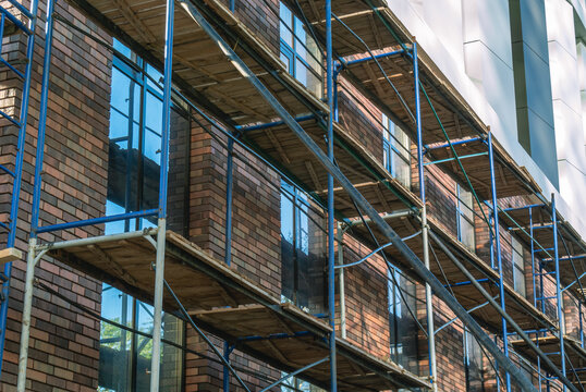 Metal scaffolding for cladding the exterior walls of the building. Decorative brick for cladding the exterior walls of the building. Installation work outside the building at a height.