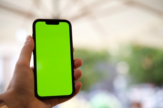Close-up of a man's hand holding a mobile phone with a vertical green screen in a restaurant, chroma key, smartphone technology, cell phone, touch display outdoors, hand
