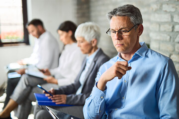 Mid adult businessman feeling worried while waiting for job interview with other candidates.