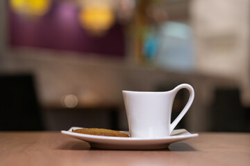 White cup filled with coffee on a plate with biscuit on beside.