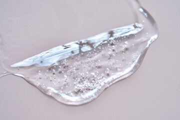 A drop of lubricant or cosmetic gel on a dusty pink background.