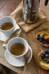 Vertical photo of two tartlets with fruit, two cups of coffee and coffee pot