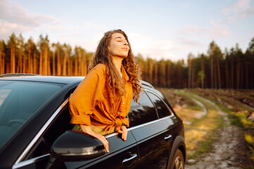 Portrait of happy young woman hang out of car window on road trip day, enjoy views and fresh air. Lifestyle, travel, tourism, nature, active life.