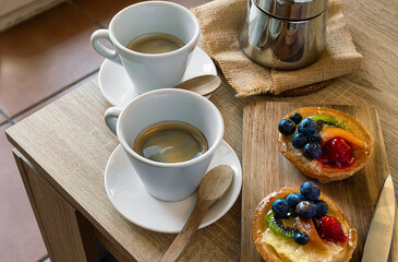 Horizontal photo of two tartlets with fruit, cup of coffee and coffee pot