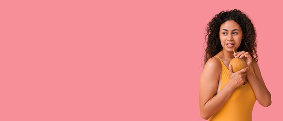 Naklejka premium Beautiful young African-American woman drinking coconut milk on pink background with space for text