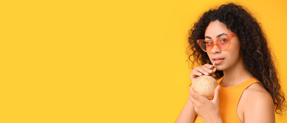 Naklejka premium Beautiful young African-American woman drinking coconut milk on yellow background with space for text