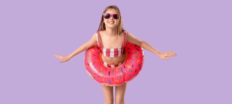 Cute little girl in swimsuit and with inflatable ring on lilac background