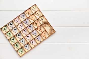 Alphabet in wooden box on white wooden background. Top view